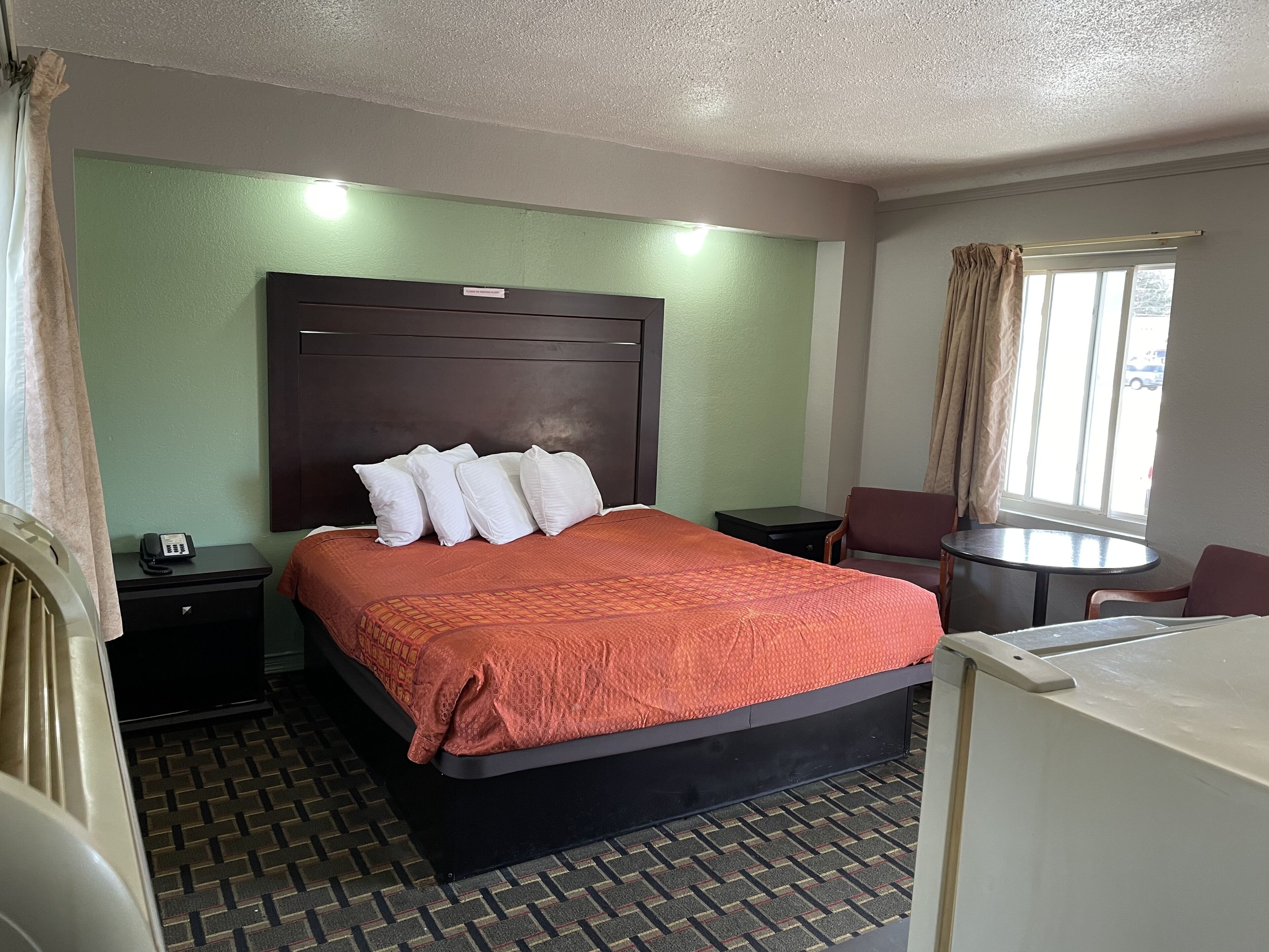 A hotel room with a large bed, a bedside table, a chair, a small table, and a window with curtains.