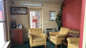 Une pièce avec deux fauteuils jaunes, une petite table, une machine à café et un panneau «Il est interdit de fumer» sur la porte.