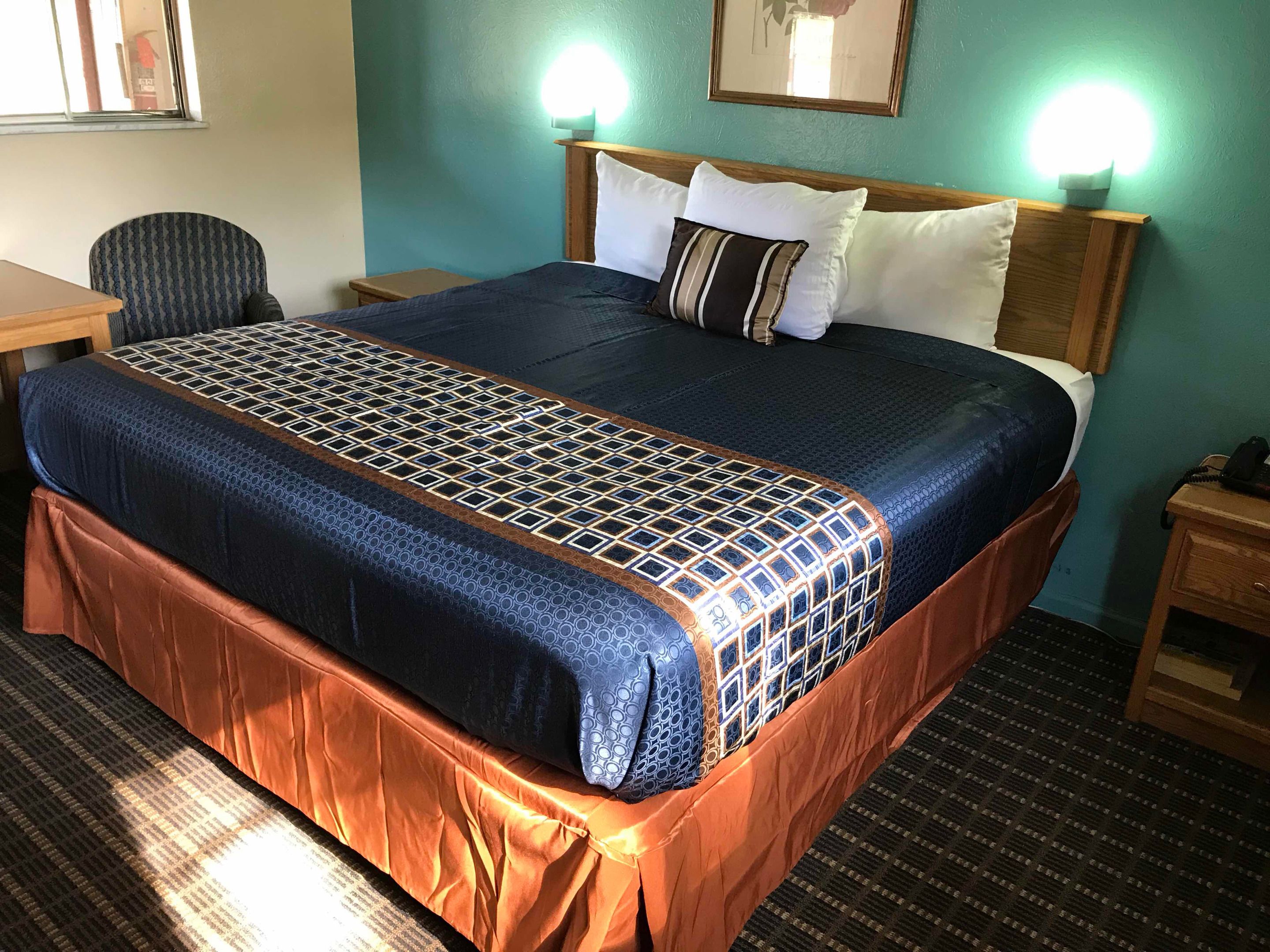 Una habitación de hotel con una cama grande, cabecera de madera, dos lámparas de noche, un escritorio y una silla.