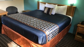 Una habitación de hotel con una cama grande, cabecera de madera, dos lámparas de noche, un escritorio y una silla.