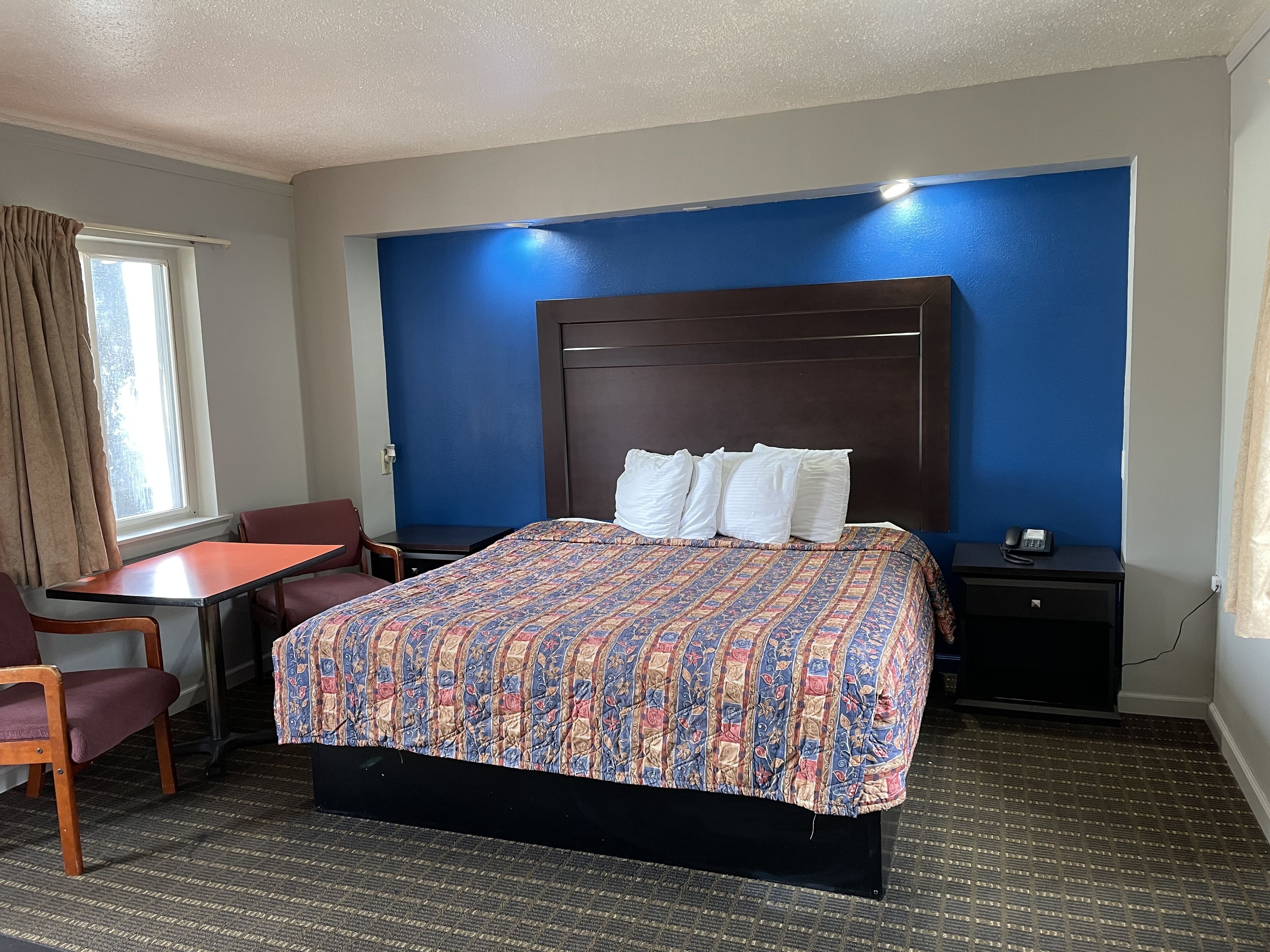 A hotel room with a large bed, a desk, a chair, a nightstand, and a window with curtains.