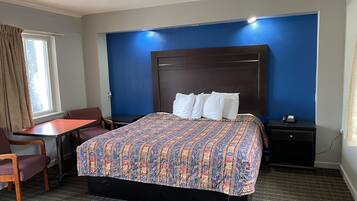 A hotel room with a large bed, a desk, a chair, a nightstand, and a window with curtains.