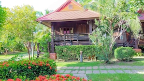 A wooden house with a porch, surrounded by lush greenery and flowering plants. - Naya Resort (Tha Yang)