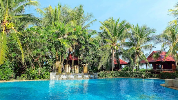 A clear blue pool surrounded by lush greenery and palm trees, with a stone structure in the center. - Naya Resort (Tha Yang)