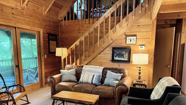 Ein gemütliches Blockhaus-Interieur mit einer Holztreppe, einem Ledersofa, einem Schaukelstuhl und einem Holztisch.