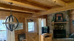 Ein Holzblockhaus mit Essbereich, Kamin, Fernseher und einer Steinwand.