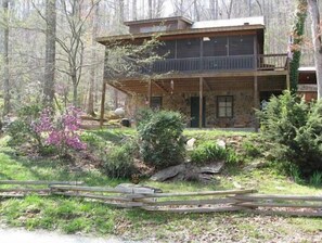 Situated in a wooded area, this cabin offers a tranquil retreat surrounded by trees and a flowering bush.