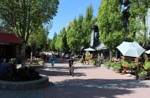 Zona peatonal con árboles, mesas al aire libre y un restaurante llamado “OBELLO”.