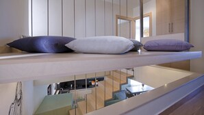 Ein modernes Interieur mit einem Holzbodenregal, das drei Kissen zeigt, einem Küchenbereich darunter und Blick in den Wohnraum.