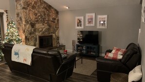 Een woonkamer met een stenen muur, een open haard, een televisie en een kerstboom.