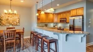 Una cocina moderna con armarios de madera, encimera de granito y refrigerador de acero inoxidable.