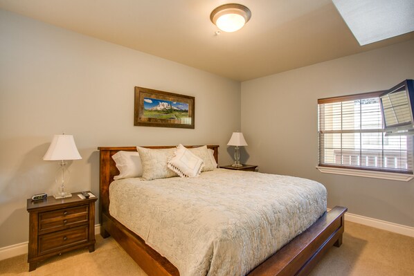 A bedroom with a large bed, two bedside tables, a nightstand, a window with blinds, and a ceiling light.