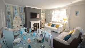 A living room with a fireplace, a white sofa, a dining table set for four, and a bookshelf. - SEASIDE COTTAGE WITH SEA VIEWS (Newbiggin-by-the-Sea)