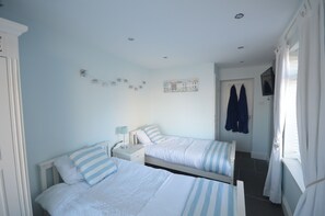 Ein Schlafzimmer mit zwei Betten, einem Nachttisch, einem an der Wand montierten Fernseher und einer Tür mit Kleiderhaken.