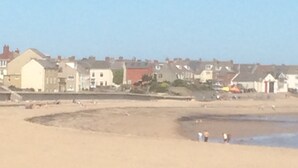 A coastal area with a sandy beach, houses in the background, and a few people near the water. - SEASIDE COTTAGE WITH SEA VIEWS (Newbiggin-by-the-Sea)