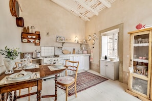 Une cuisine avec des meubles de rangement en bois, une table à manger dressée pour deux personnes et un tapis rouge à motifs.
