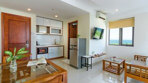 A modern kitchen with a built-in microwave, refrigerator, and a dining area with a wooden table and chairs. - Salamander Hotel and Apartment (Da Nang)