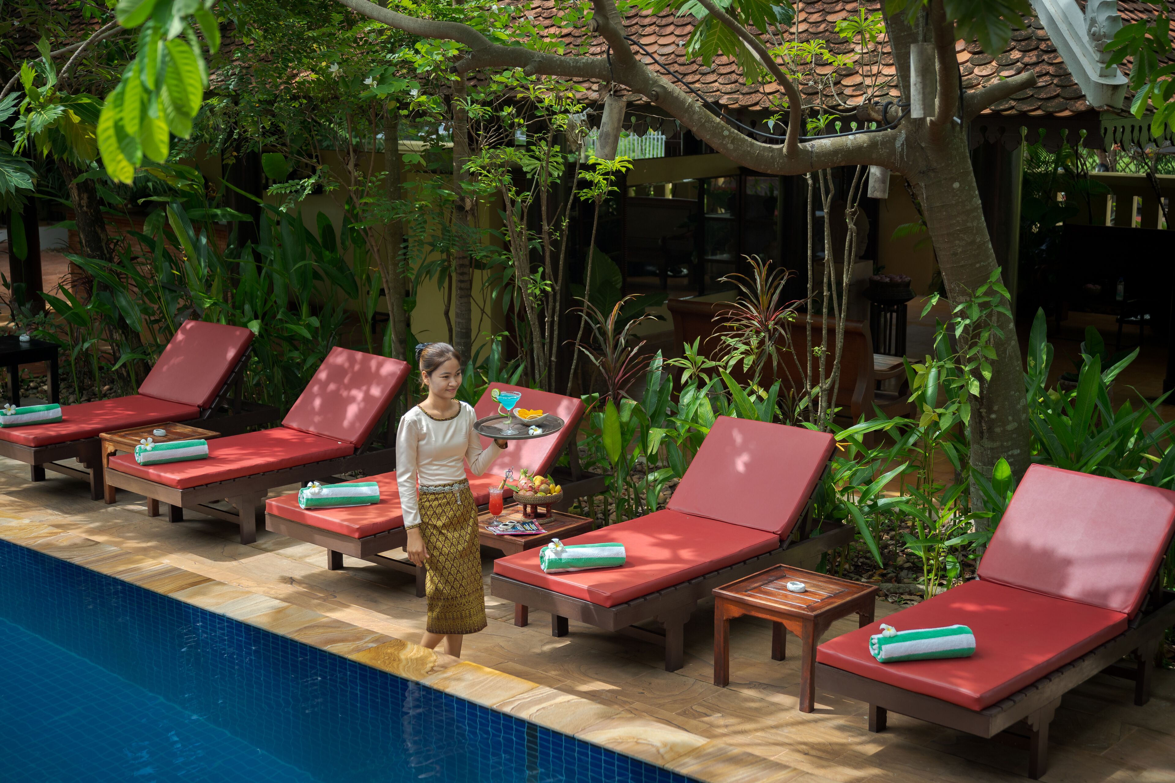 Una zona junto a la piscina con sillas reclinables rojas, una piscina y abundante vegetación.