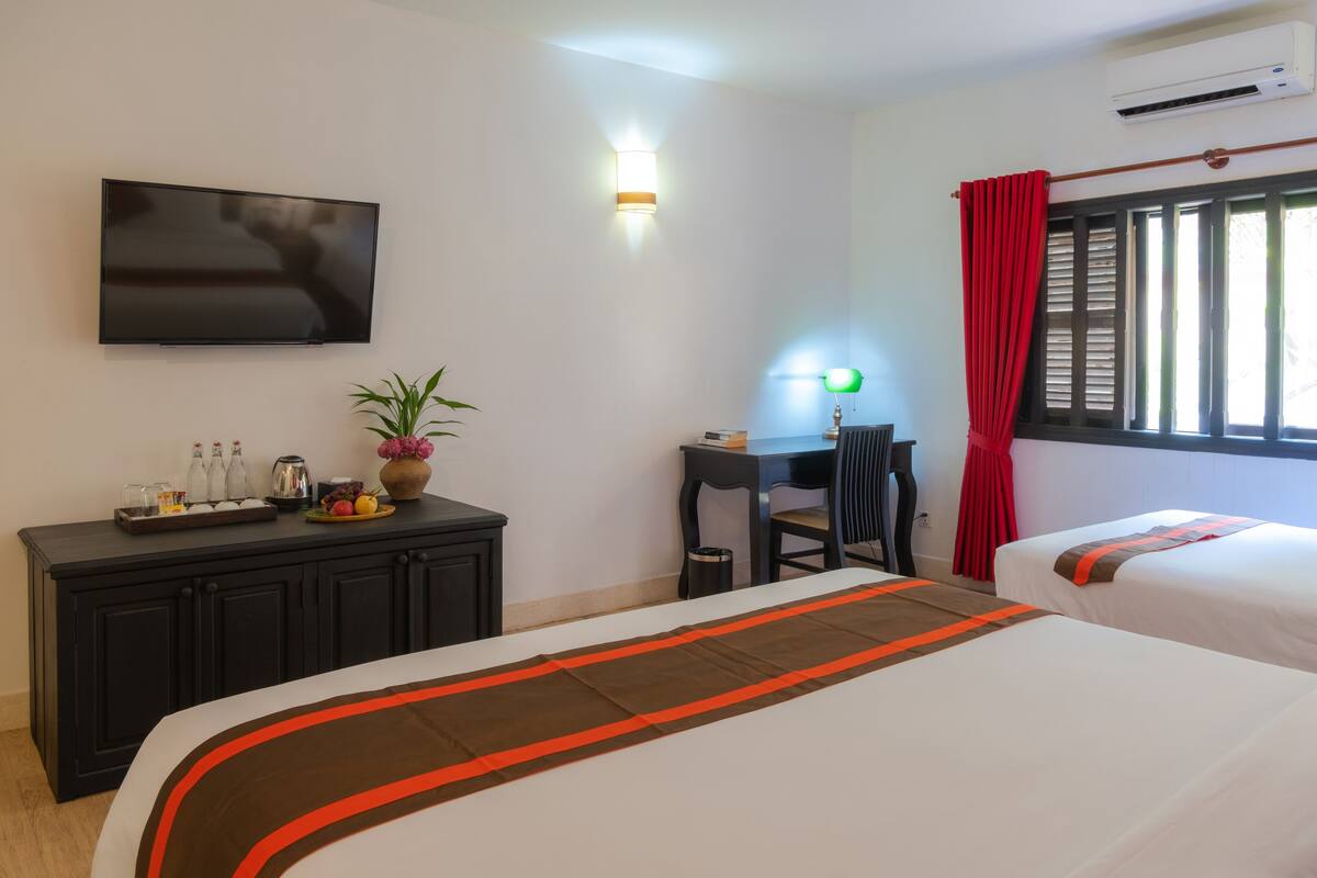 A hotel room with two beds, a desk, a TV, and a window with curtains.