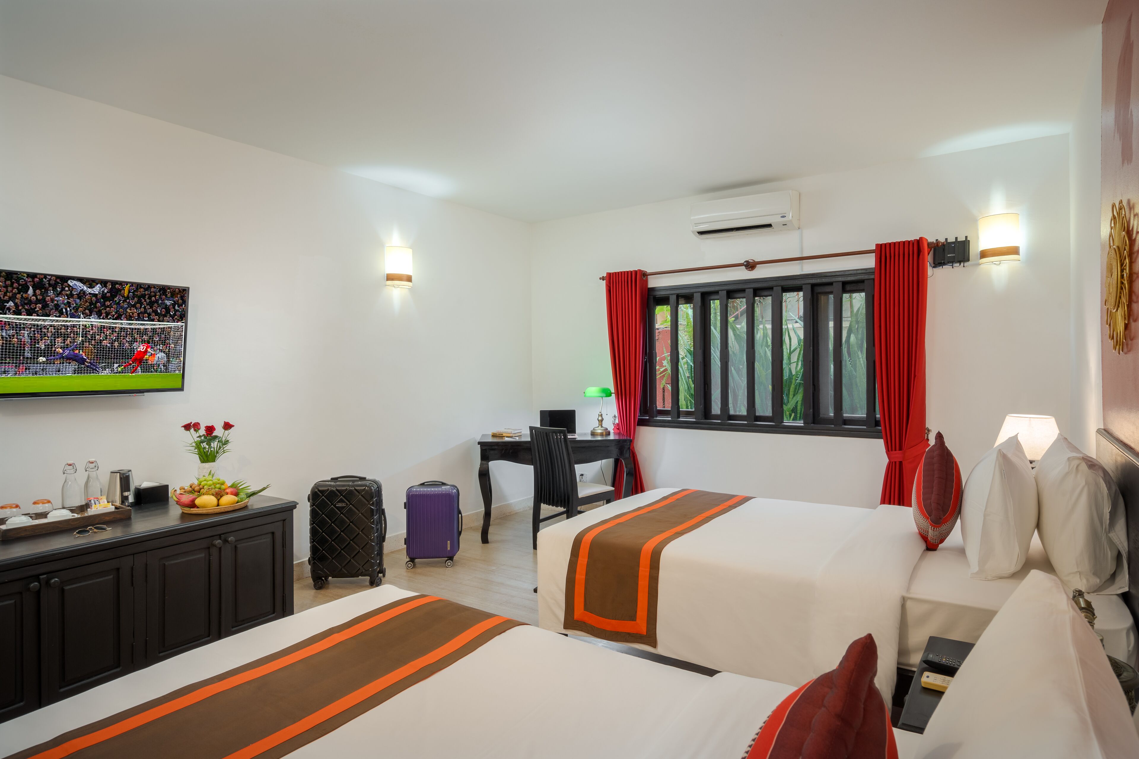 A hotel room with two beds, a desk, a chair, a TV, and a window with curtains.