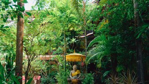 A statue of a seated figure in a lush garden setting with a thatched umbrella. - Pandora Suite D'Angkor (Siem Reap)