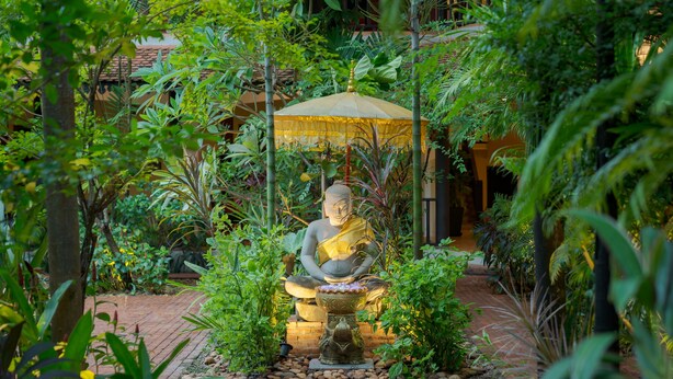 A statue of a seated figure in a garden setting with a tiled floor and surrounding greenery. - Pandora Suite D'Angkor (Siem Reap)