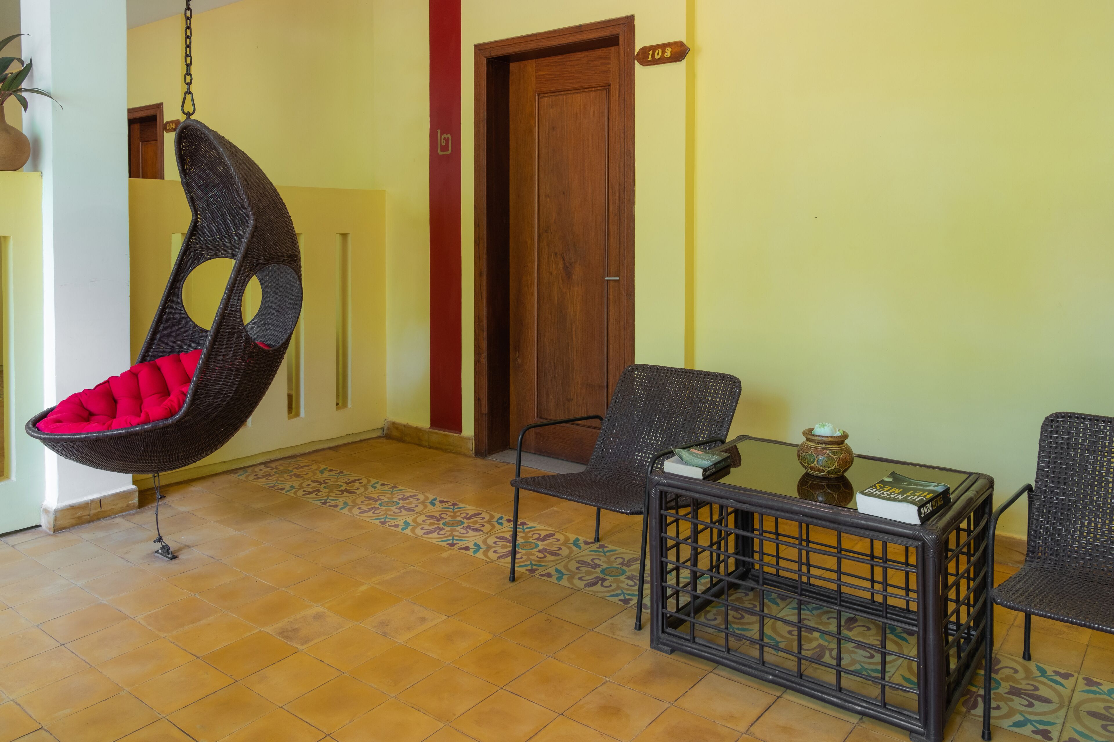 Une pièce avec un fauteuil suspendu, une table sur laquelle se trouve un livre et une porte portant le numéro 108.