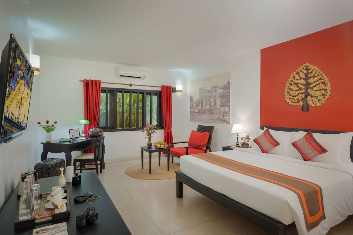 A hotel room with a bed, a desk, a chair, a table with a tray, and a window with curtains.