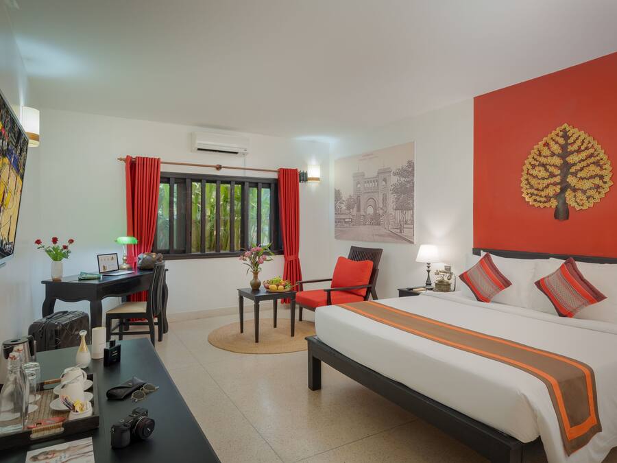 A hotel room with a bed, a desk, a chair, a table with a tray, and a window with curtains.