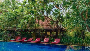 A swimming pool with red lounge chairs and a covered seating area surrounded by lush greenery. - Pandora Suite D'Angkor (Siem Reap)