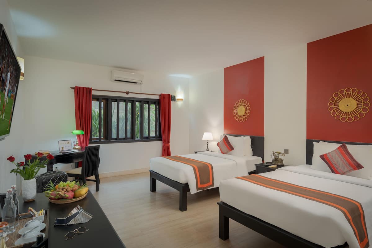 A hotel room with two beds, a desk with a computer, a chair, and a dining table with a fruit bowl.