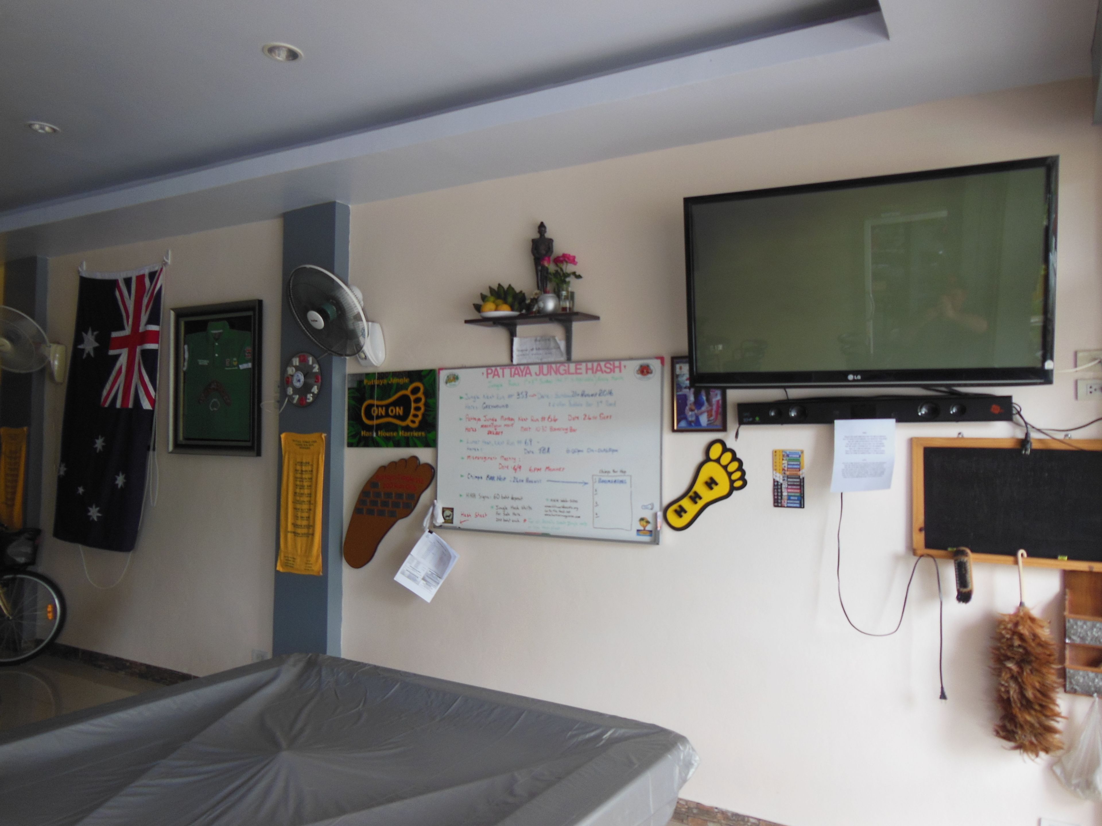 A room with a bed, a television, a whiteboard, and various wall decorations including a flag, a shoe, and a handprint.