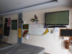 A room with a bed, a television, a whiteboard, and various wall decorations including a flag, a shoe, and a handprint. - Boomerang Guesthouse (Pattaya)