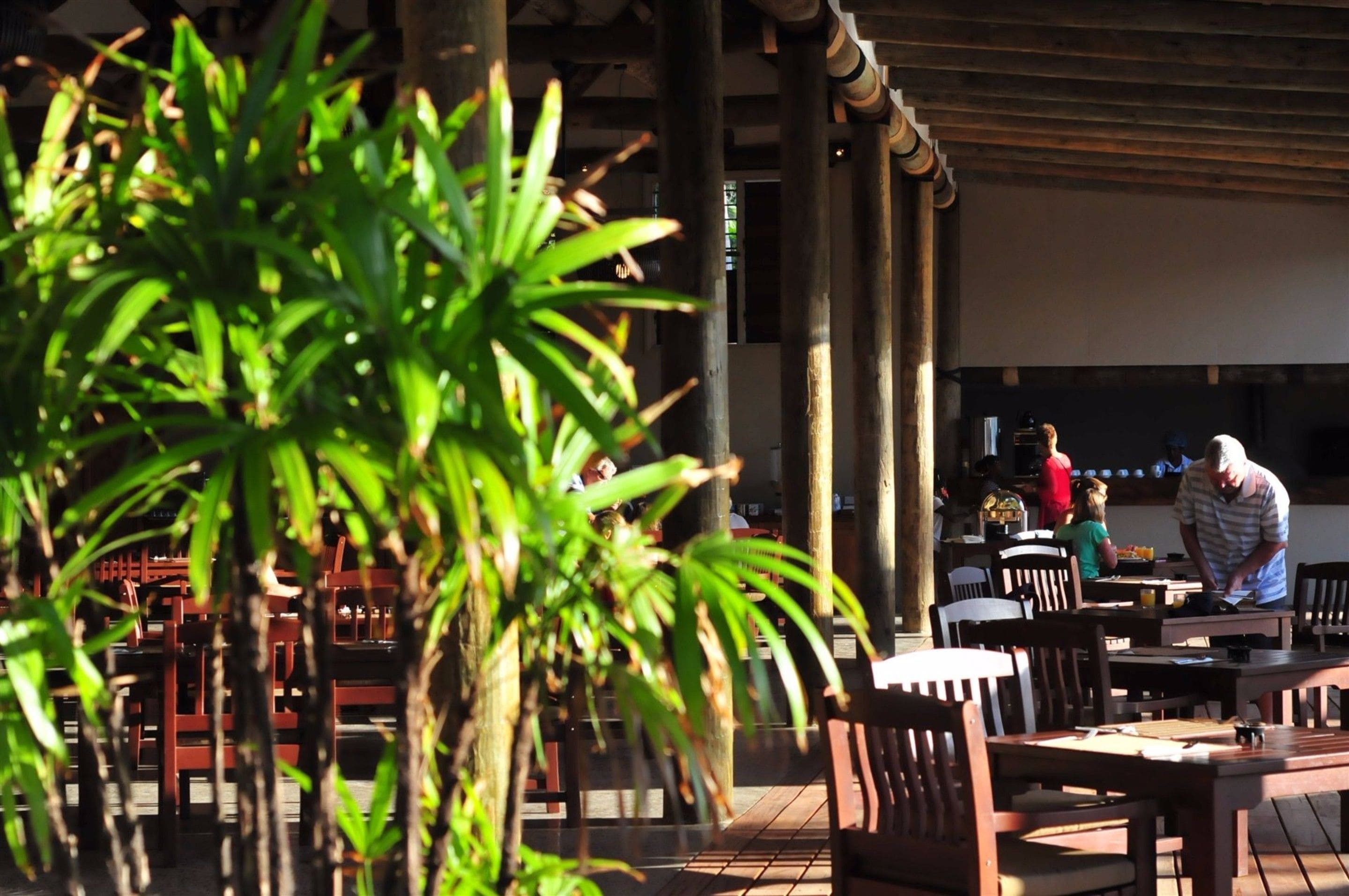 An outdoor dining area with wooden tables and chairs, surrounded by potted plants.