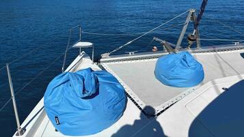 Cubierta de barco con una lona azul, barandales de metal y vista al mar y una isla boscosa.