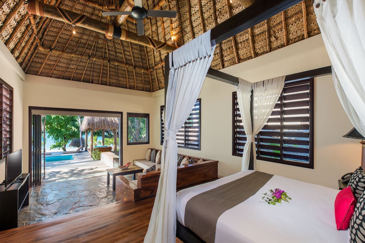 A spacious bedroom with a large bed, a TV, and a view of the pool.