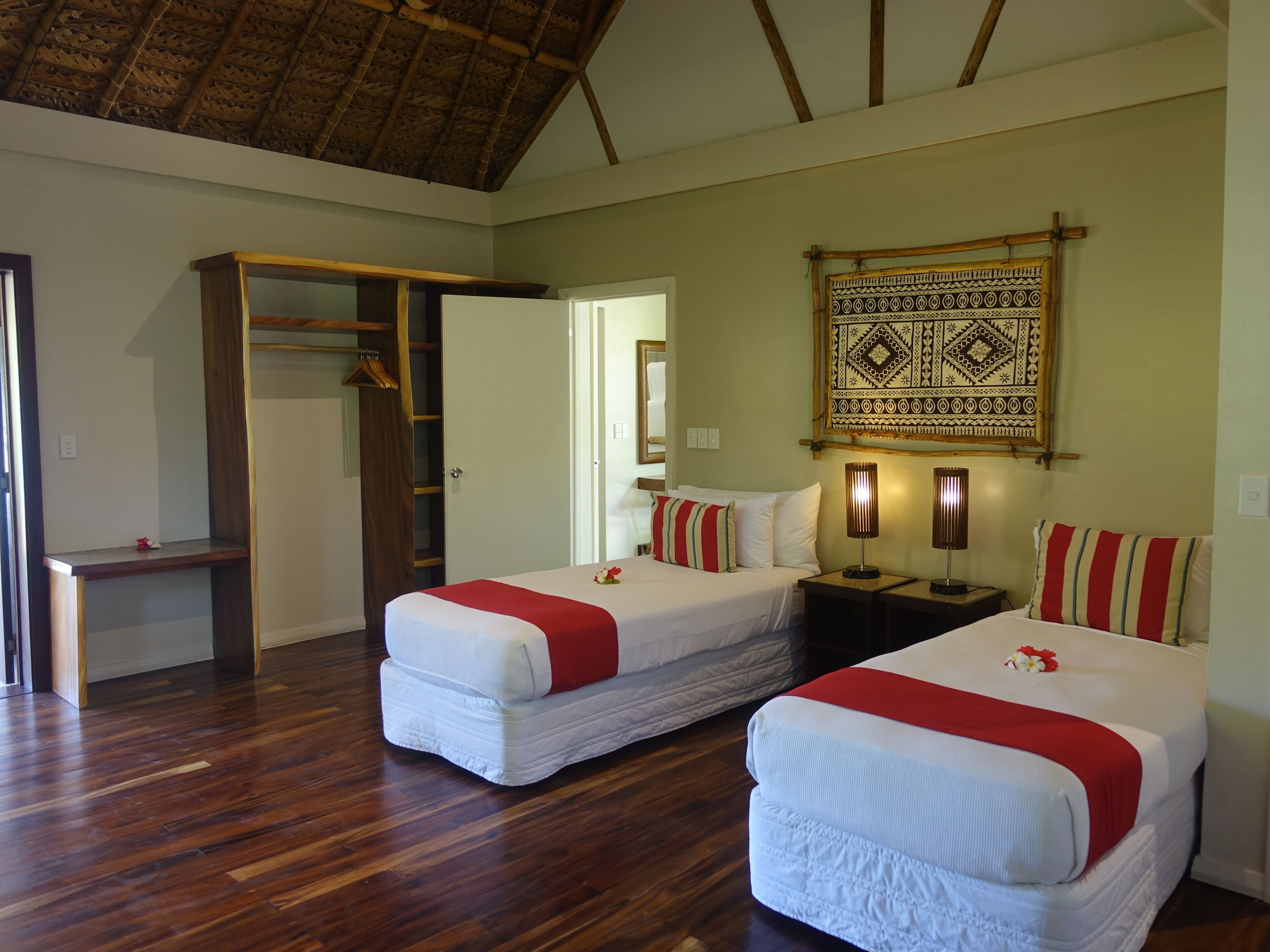 A hotel room with two beds, wooden flooring, a wardrobe, and a patterned tapestry on the wall.