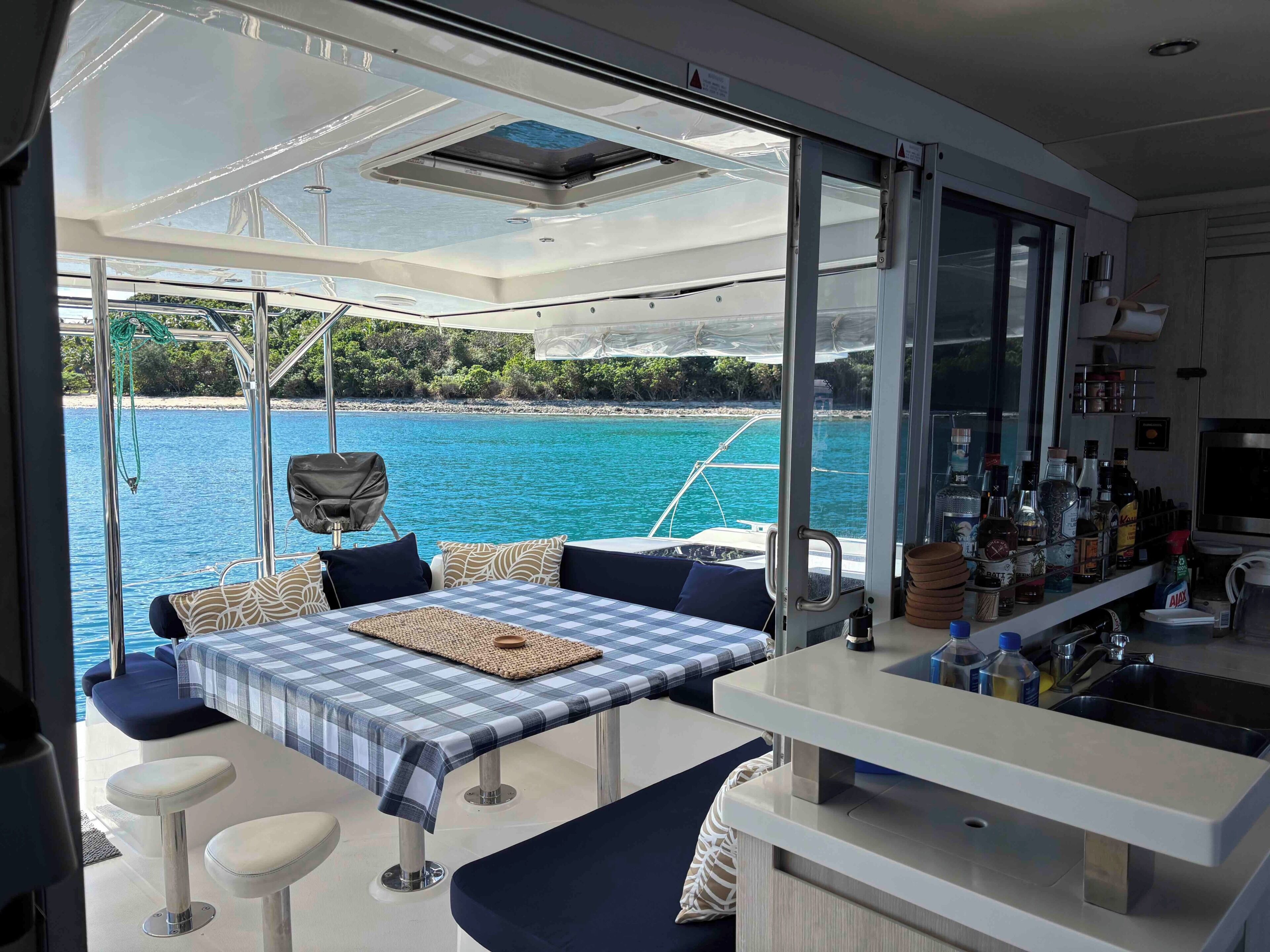 A modern boat interior with a dining area, bar, and large windows offering a view of the sea.