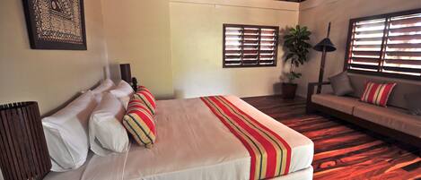 Un dormitorio con una cama grande, un sofá, una planta en maceta y un techo con diseño tejido.