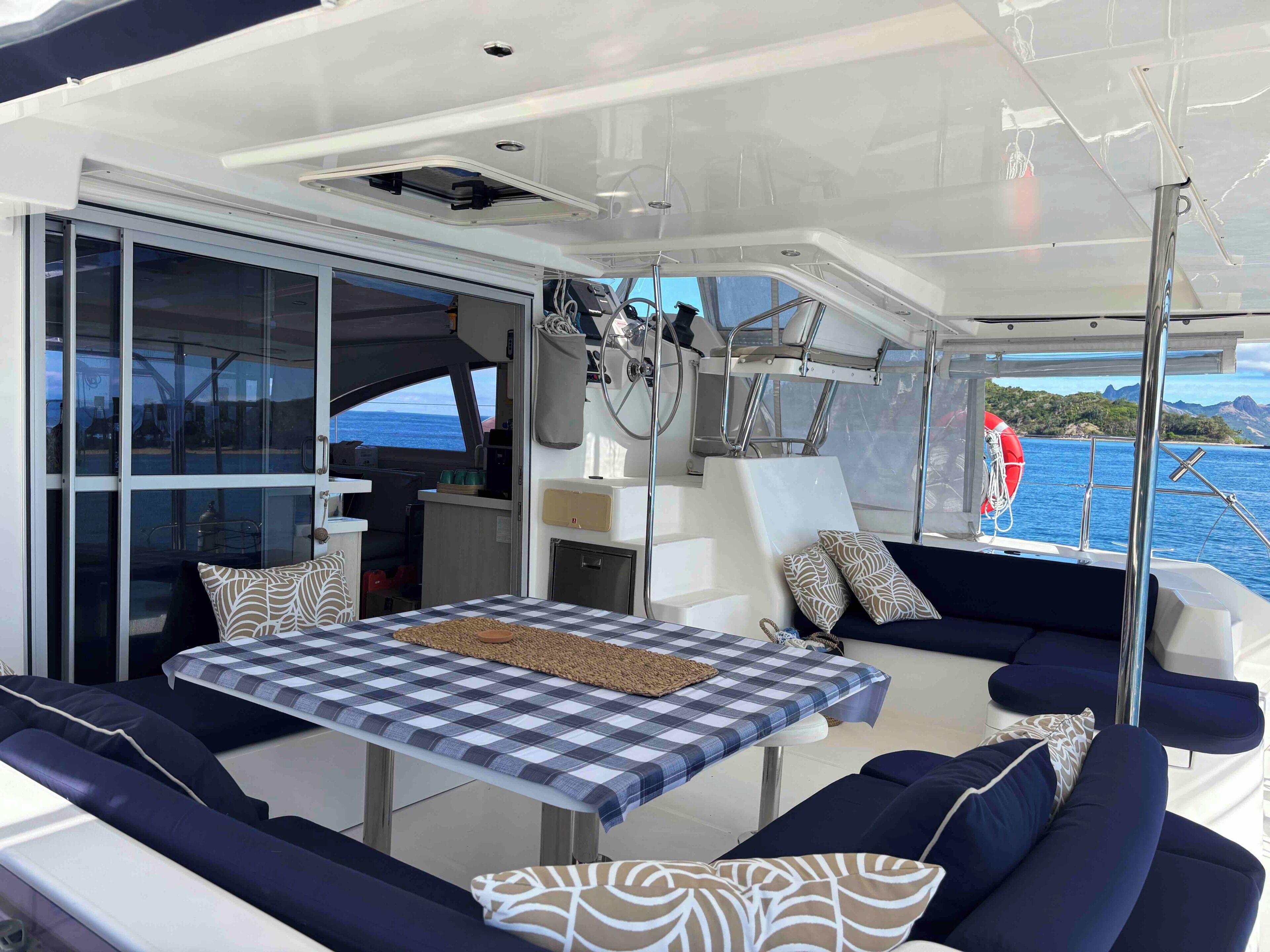 Interior de barco con comedor, asientos y vista al mar.