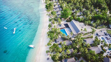 Vista aérea de un complejo turístico con playa, piscina y varias edificaciones tipo bungalow rodeadas de palmeras.