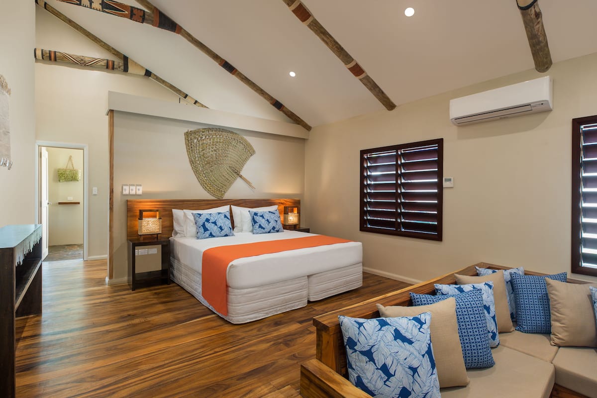 A bedroom with a large bed, wooden flooring, a sofa, and a ceiling with exposed beams.