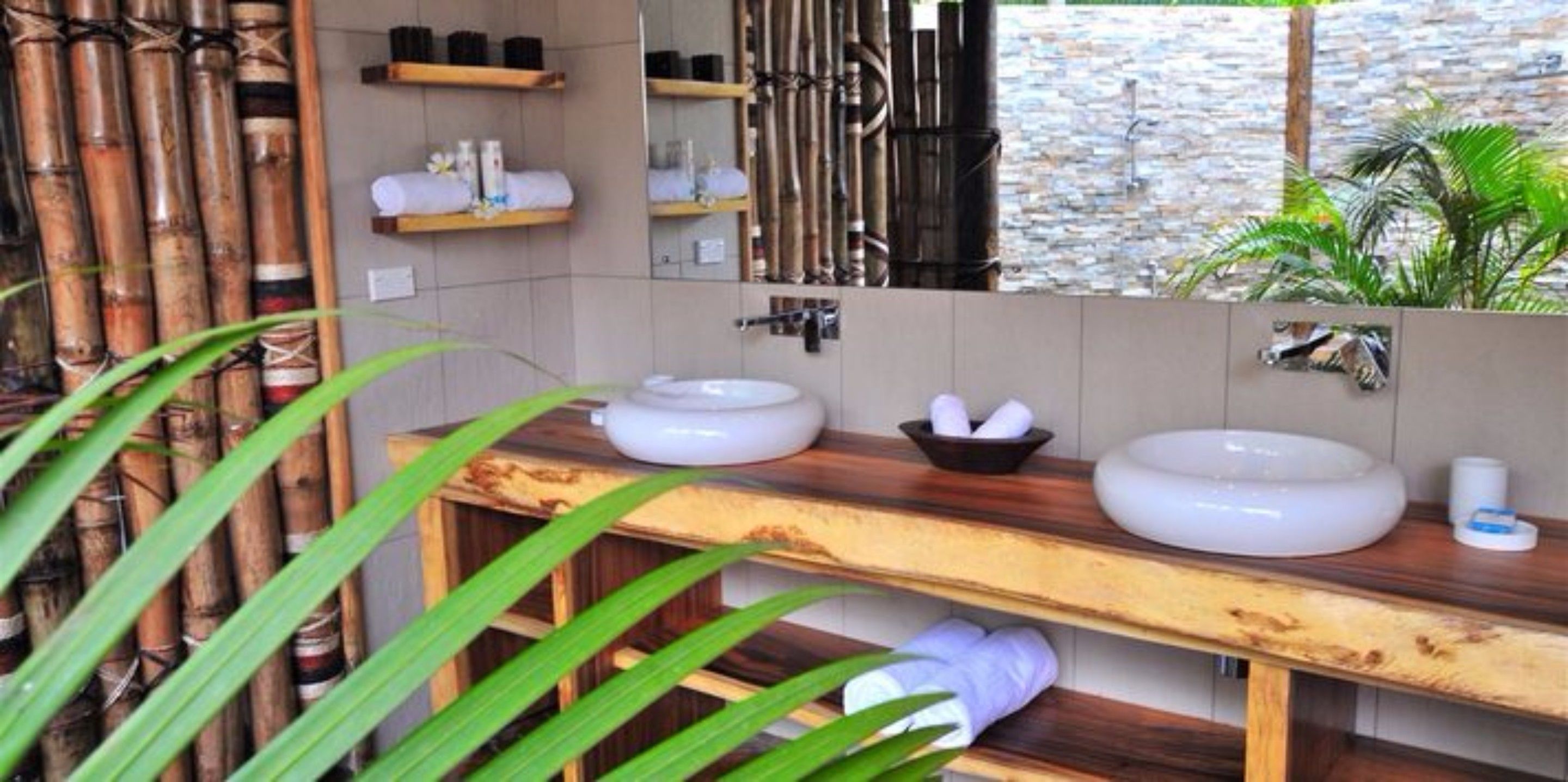 A bathroom with two sinks, wooden shelves, a mirror, and a stone wall.