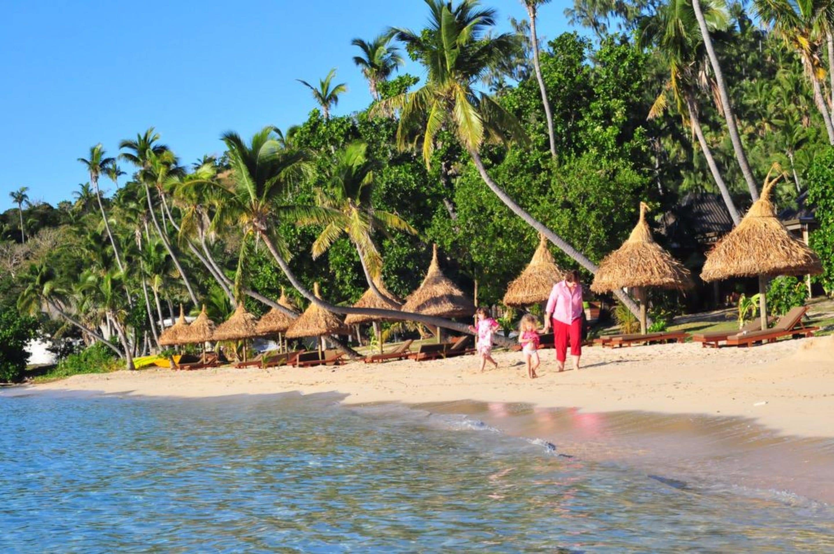 A beach with thatched-roof huts and palm trees.