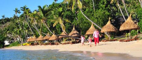 A beach with thatched-roof huts and palm trees.