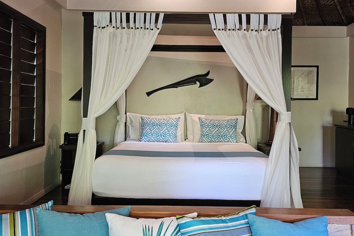 A spacious bedroom with a large bed, white curtains, and a unique wall decoration.