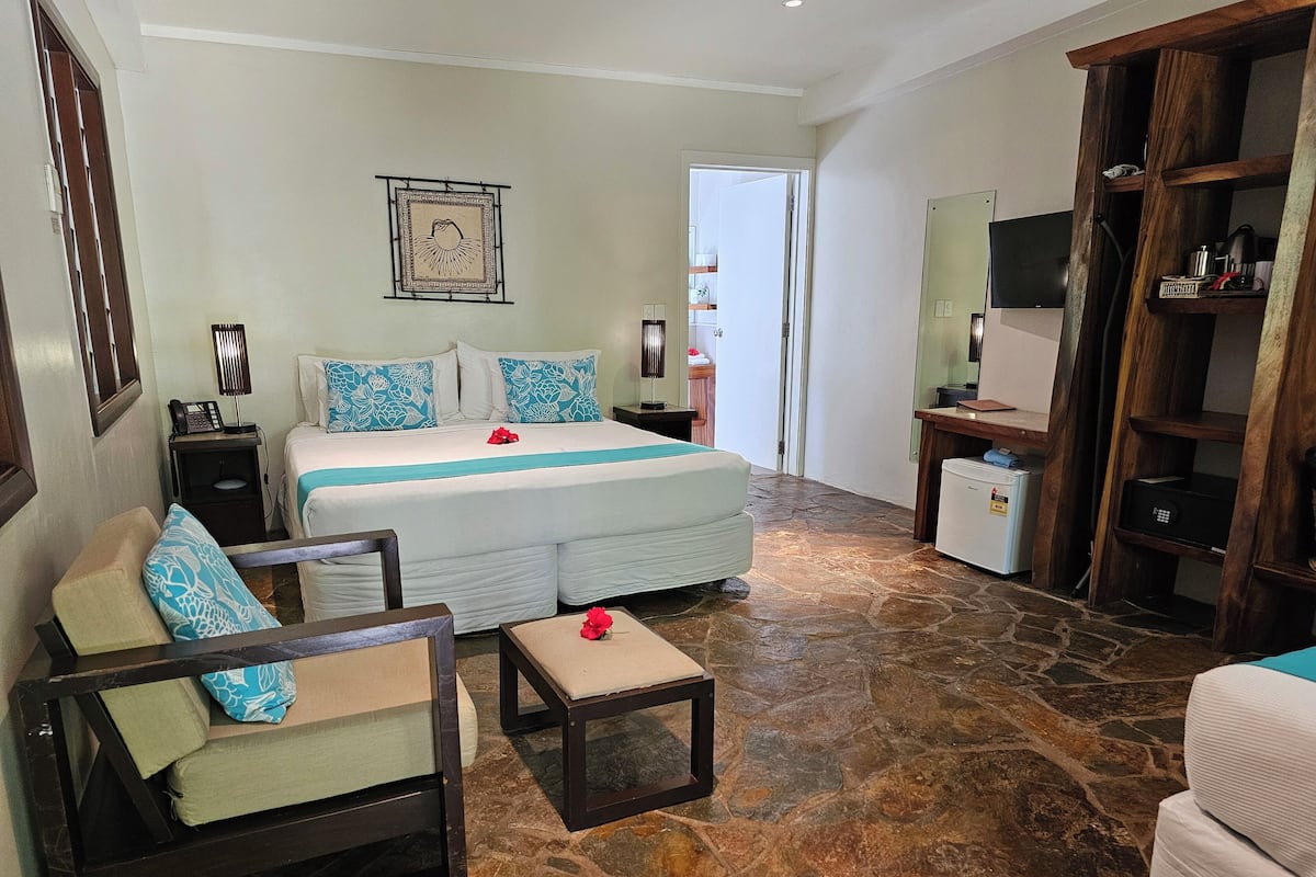A hotel room with a bed, a sofa, a small table, a TV, and a kitchenette.