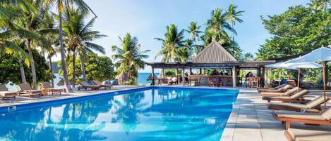 Une piscine entourée de palmiers, avec des chaises longues et un kiosque.
