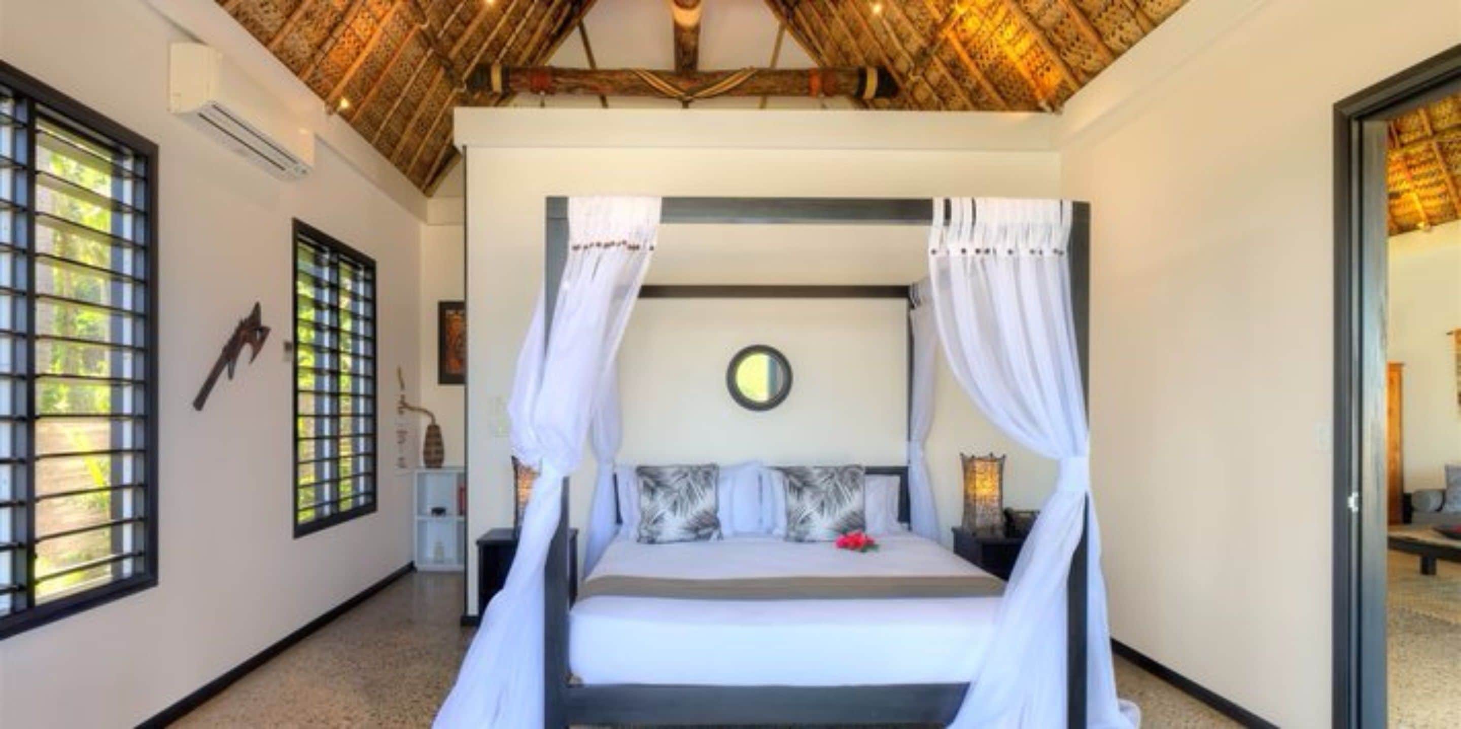 A bedroom with a canopy bed, a round mirror on the wall, and a view of the outdoors through the window.