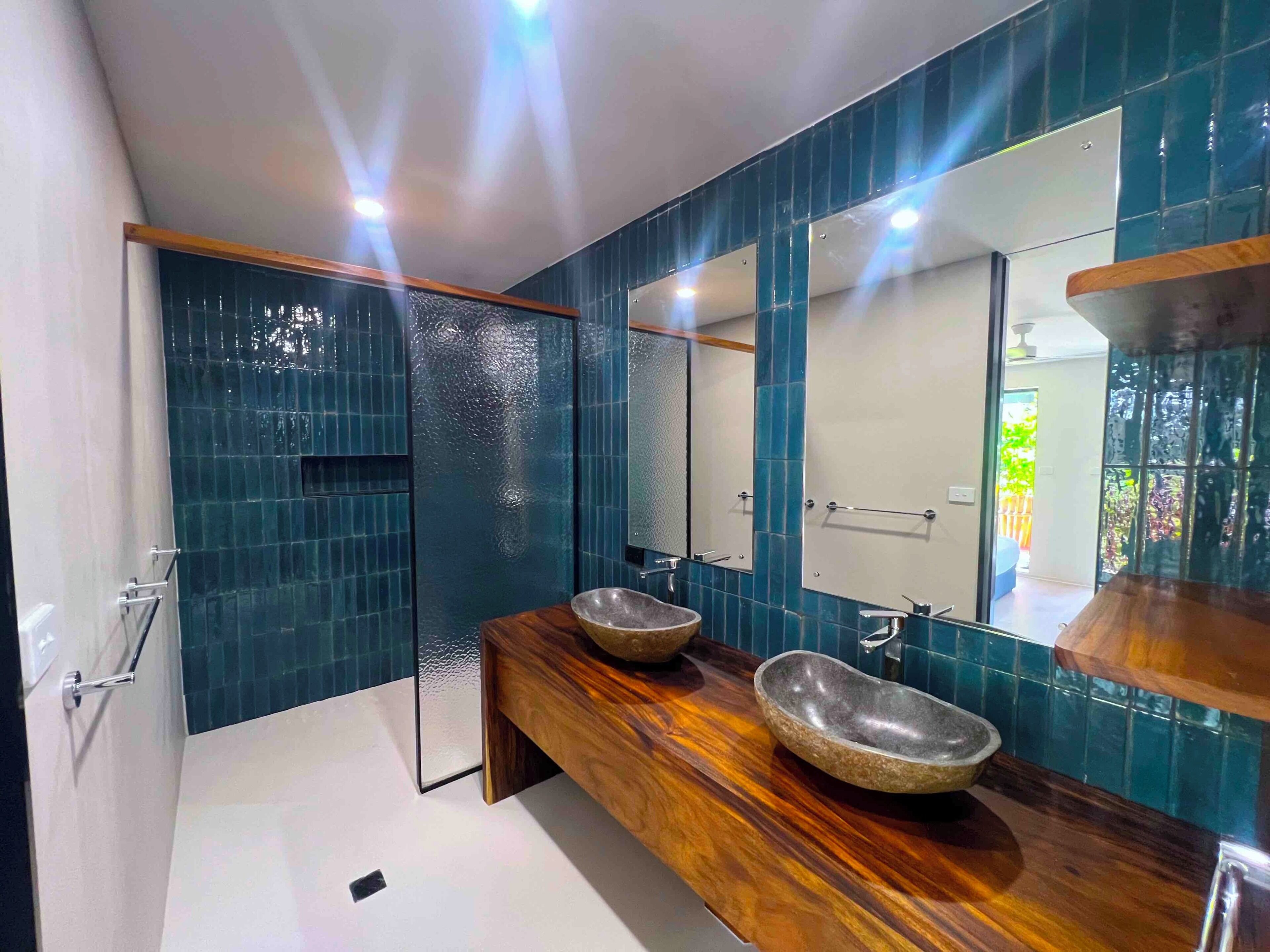 A modern bathroom with a wooden vanity, two stone sinks, and a large mirror.